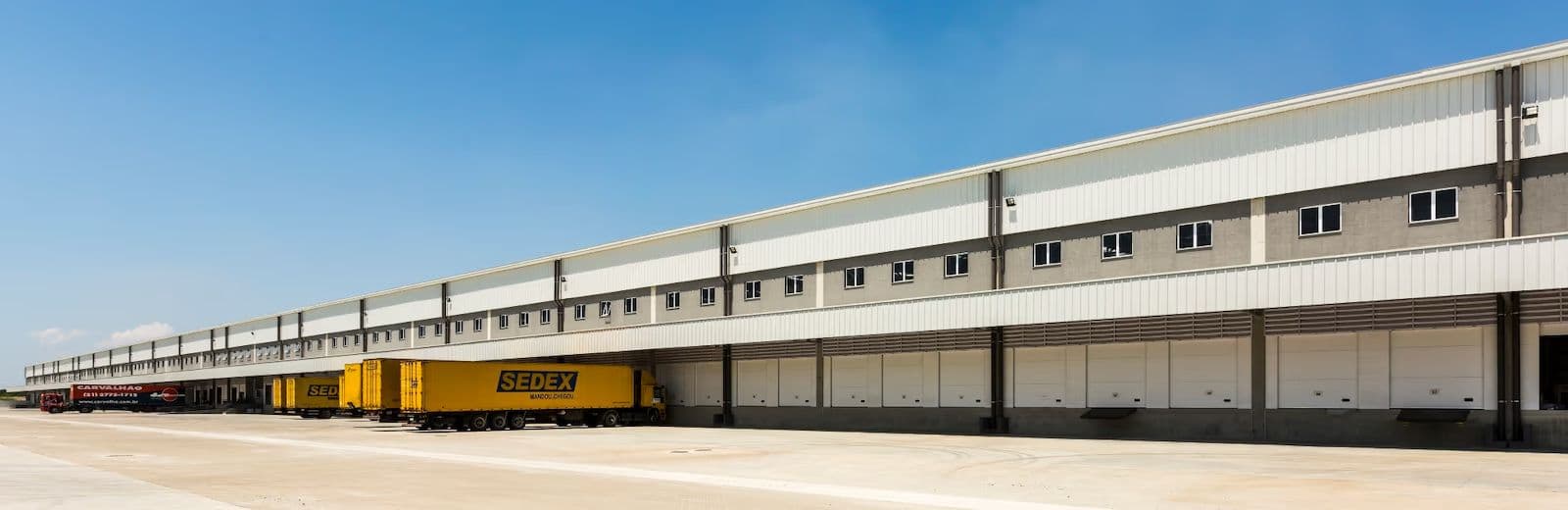 Fachada de galpão logístico com sequência de docas de carregamento e carretas
